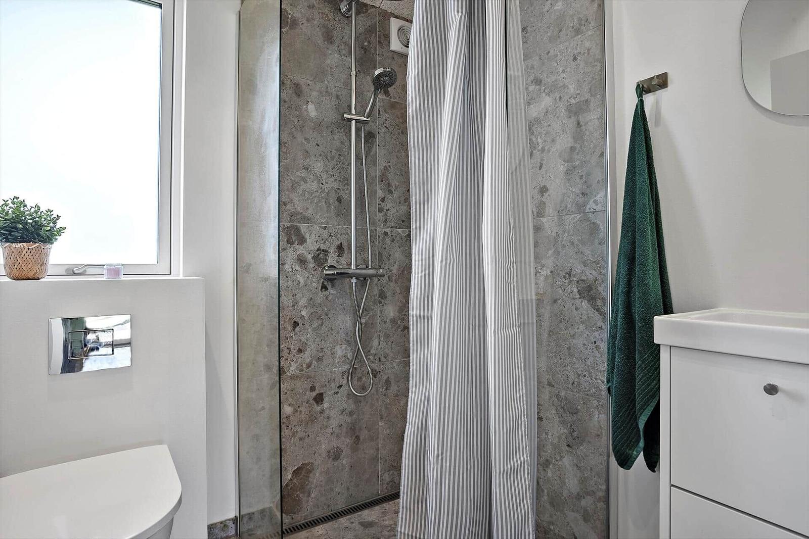 Dusche mit Glaswand, Steinwand und Streifentuch. Toilette und Waschbecken daneben.