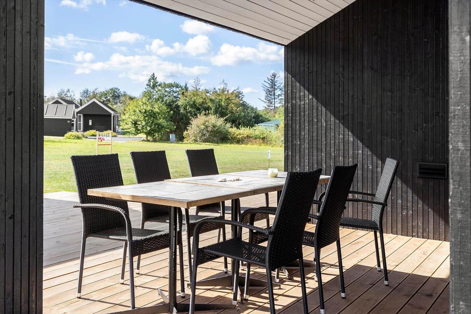 Terrasse mit Tisch und sechs Stühlen, Blick auf grünes Gelände und Himmel.