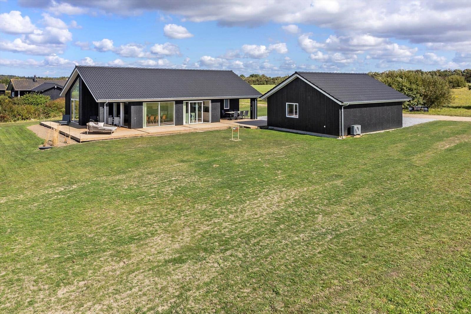 Moderne schwarze Villa mit großem Garten und Terrasse. Einzelne Gebäude mit Glasfronten.