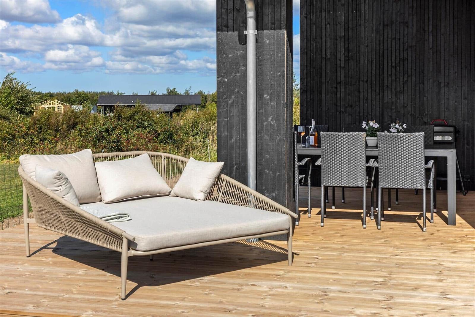 Terrasse mit Liege, Tisch und Stühlen. Holzdecke und schwarze Wand.