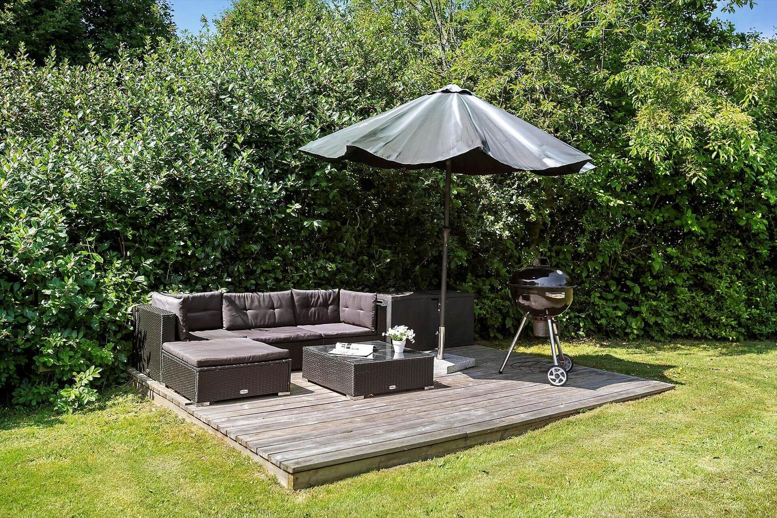 Deck with seating, umbrella, and grill. Surrounded by greenery.