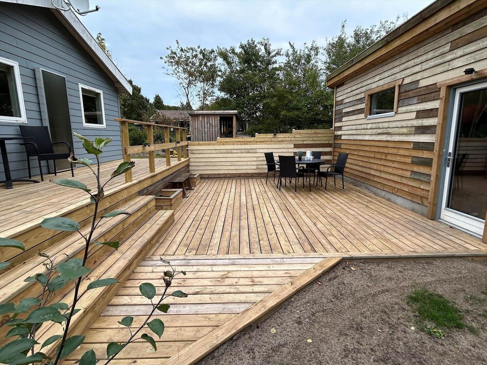 Wooden terrace with seating area and stairs between two houses.