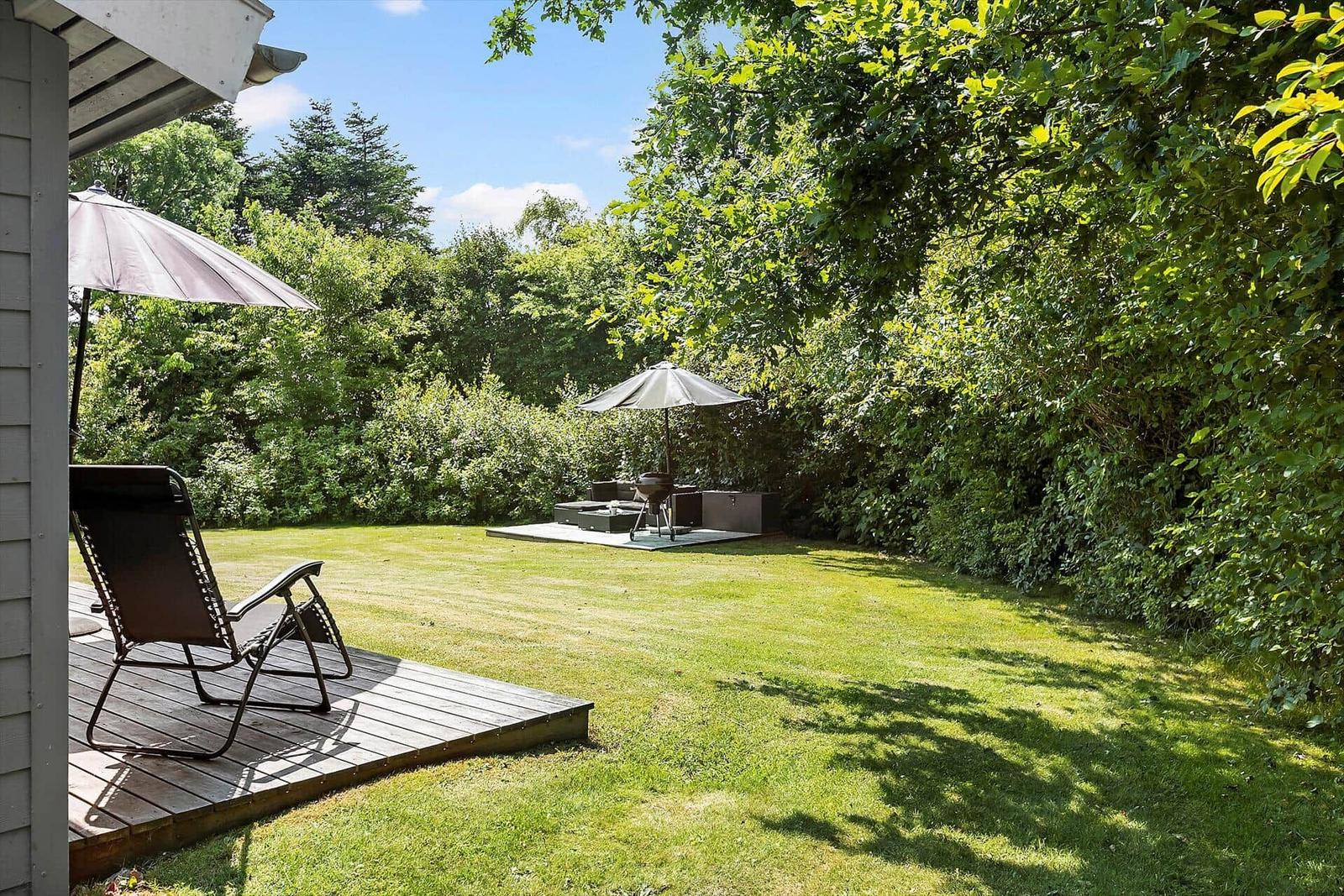 Deck with lounge chair and umbrella. Lawn and seating area in the background.