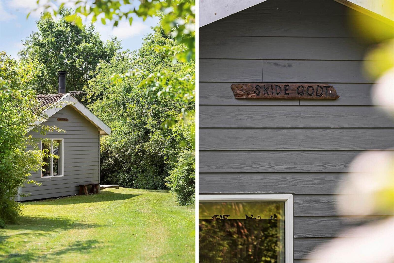 A small house with wooden siding and a sign reading SKIDE GODT.