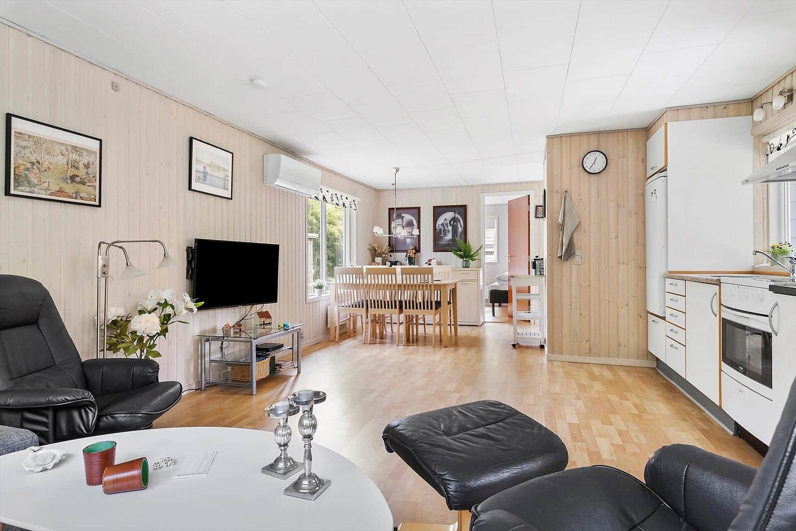 Living room with kitchen and dining area. Wooden walls, black chairs, and white table.