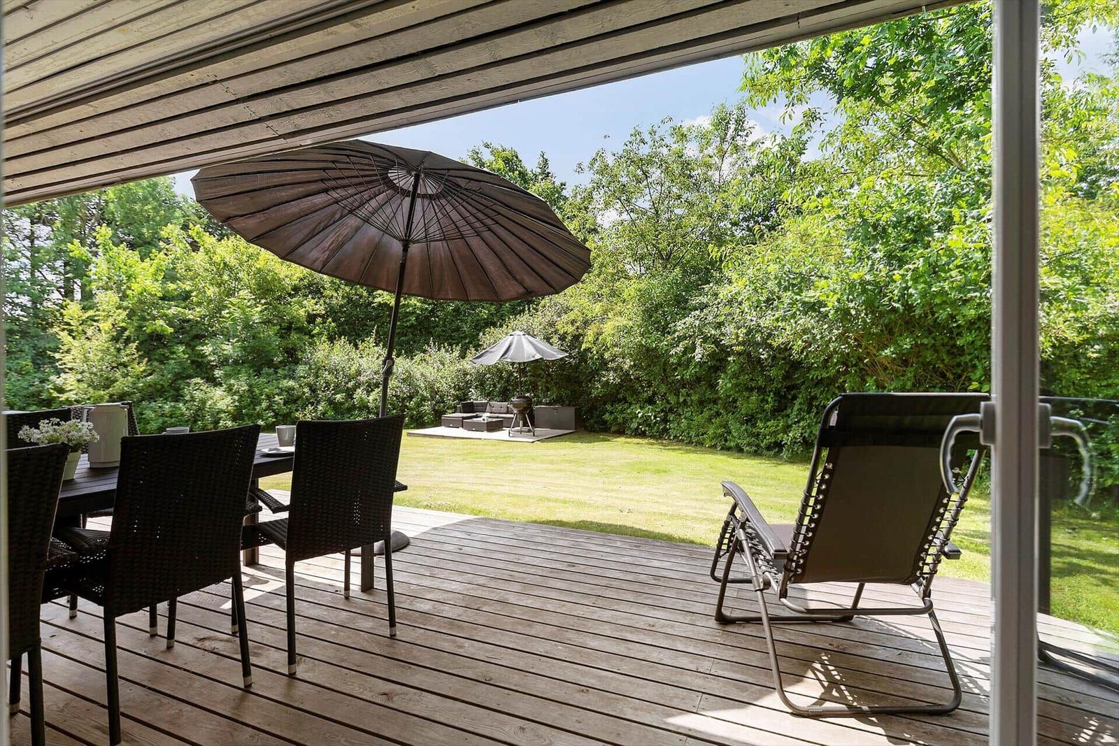 Terrace with table, chairs, and umbrella. Lawn and garden furniture in the background.