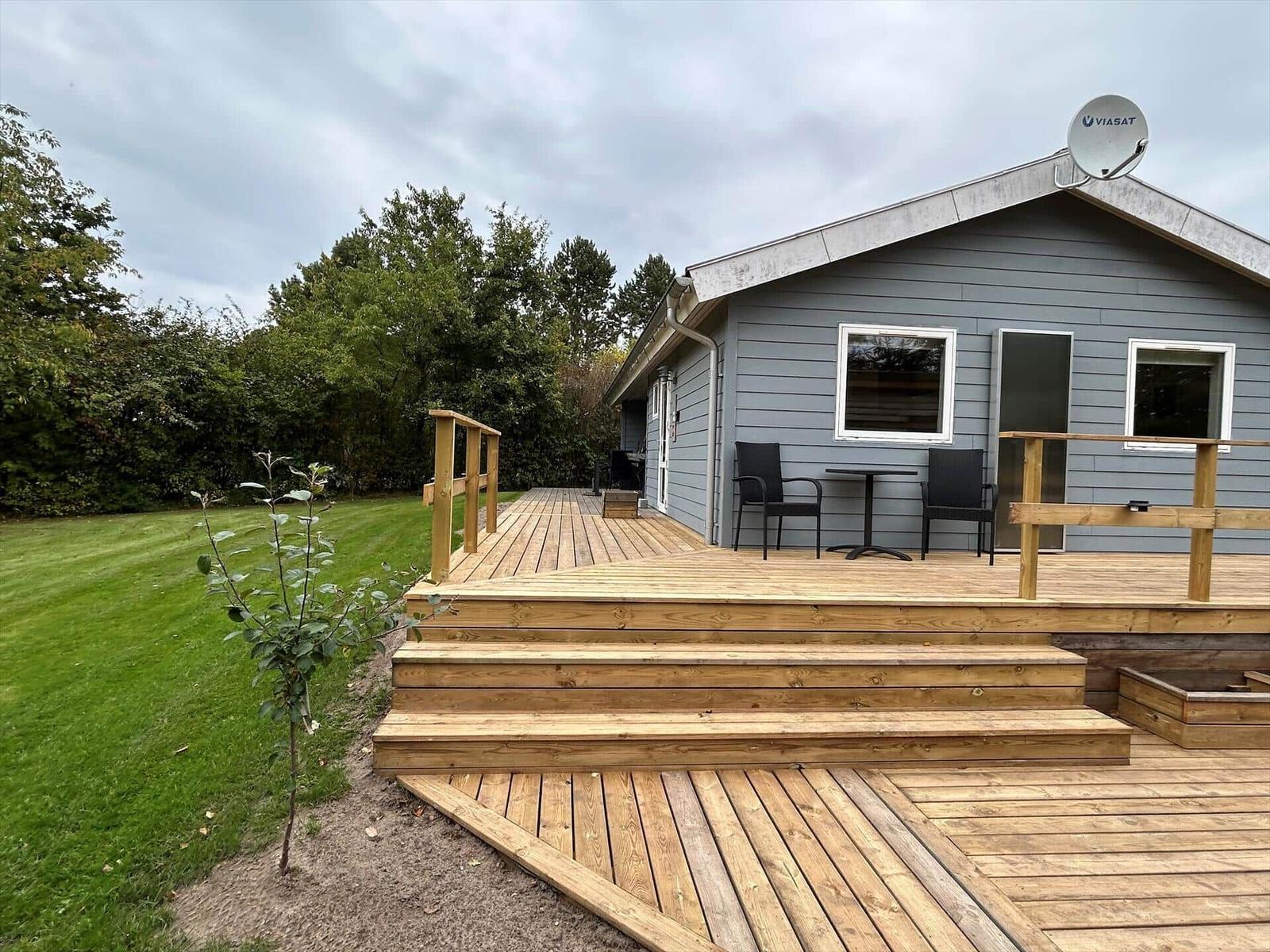 Gray holiday home with wooden terrace and garden. Satellite dish on roof.