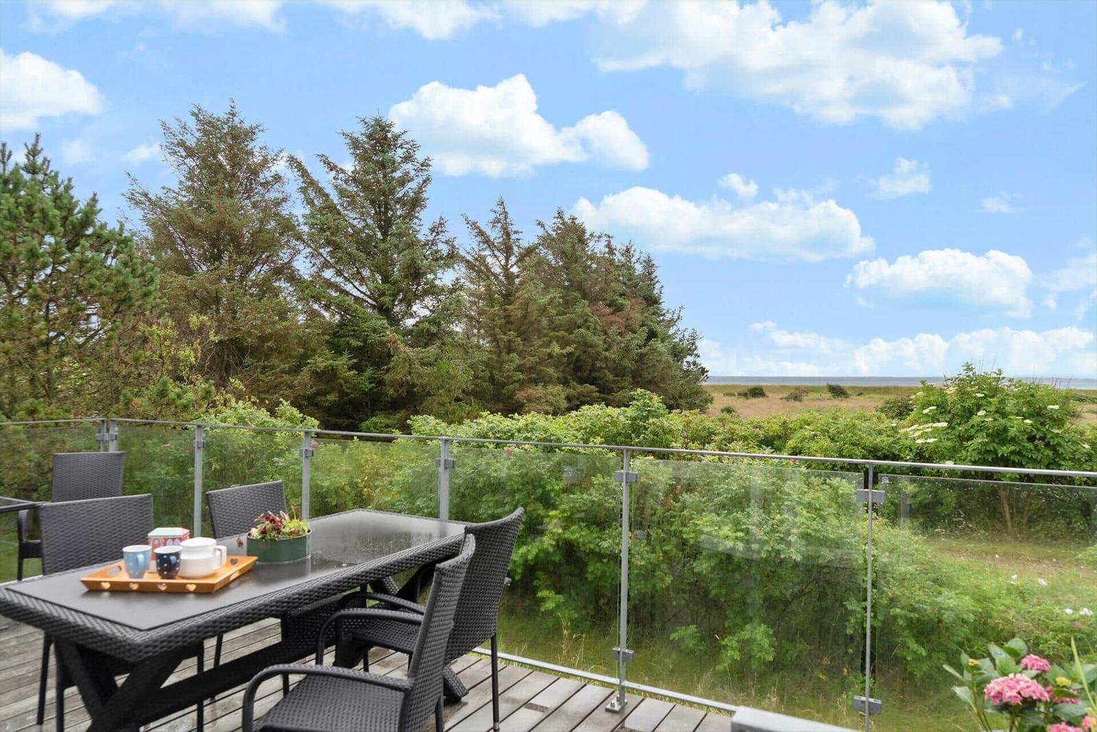 Terrasse mit Tisch und Stühlen, Blick auf Grünflächen und Meer.