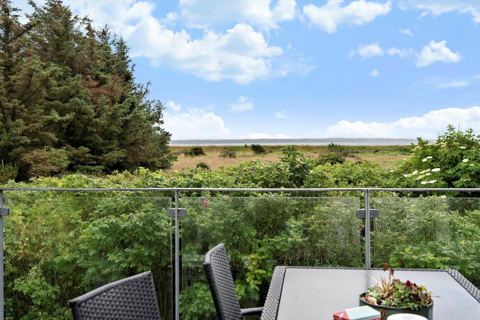 Terrasse mit Tisch und Stühlen, Blick auf Grünflächen und Wasser.