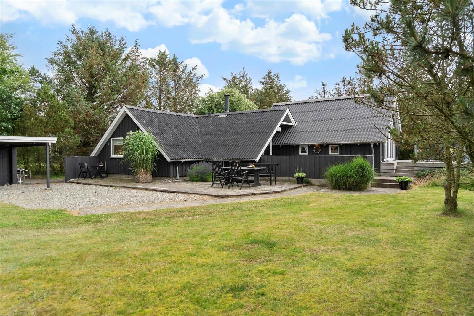 Ein dunkles Holzhaus mit Terrasse und Garten. Außentische und Stühle sind vorhanden.