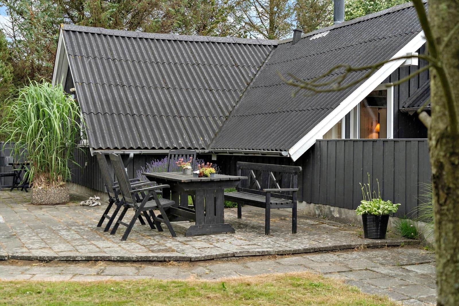 Terrasse mit Tisch, Stühlen und Bank vor einem Haus mit dunklem Holz und Schieferdach.