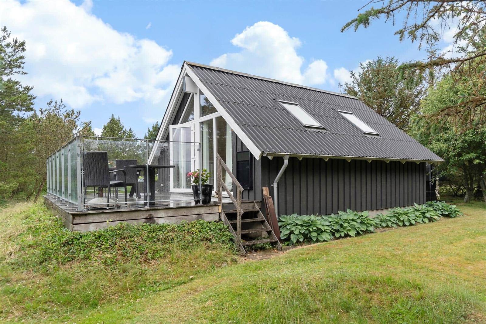 Moderne Hütte mit Terrasse und Glasgeländer in grüner Umgebung.