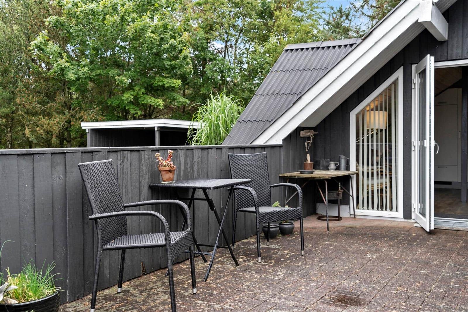 Terrasse mit Tisch und zwei Stühlen, angrenzend an ein Haus mit offener Tür.
