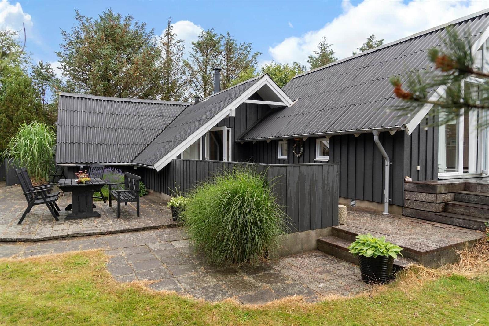 Haus mit dunkler Holzfassade und Terrasse mit Gartenmöbeln.
