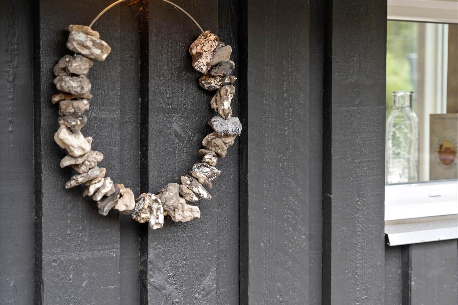 Ein Kranz aus Muschelschalen hängt an einer dunklen Holzwand.