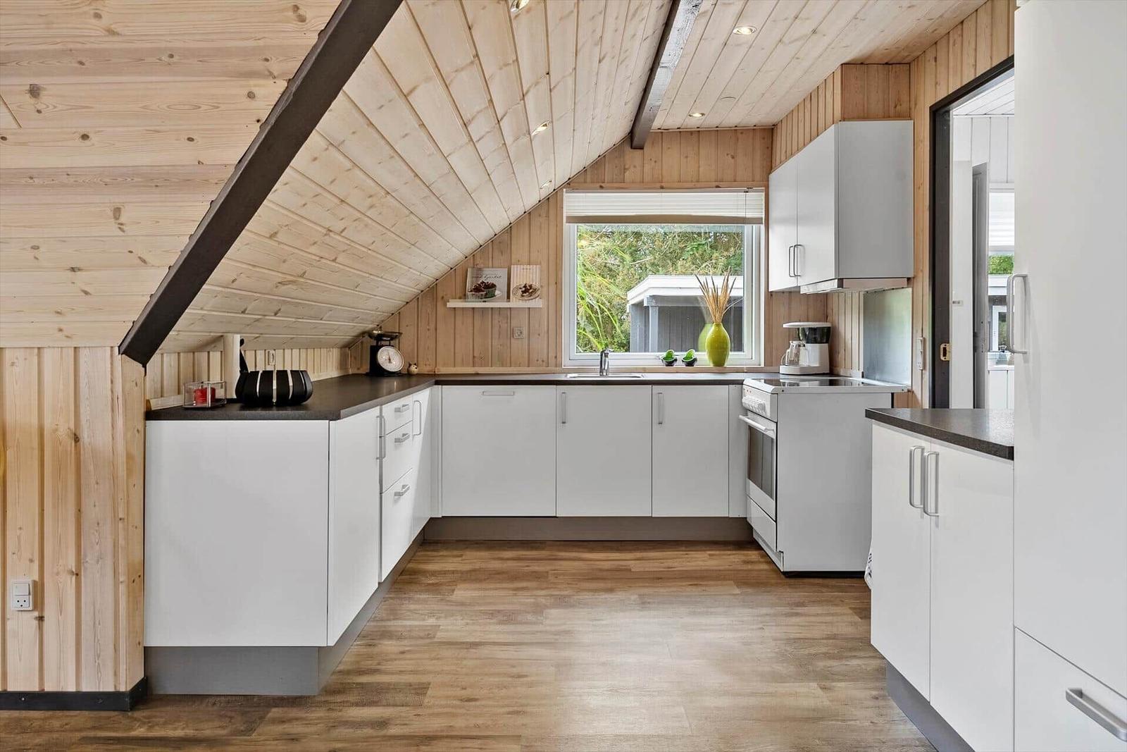 Küche mit weißen Schränken, Holzdecke und Fenster mit Blick nach draußen.