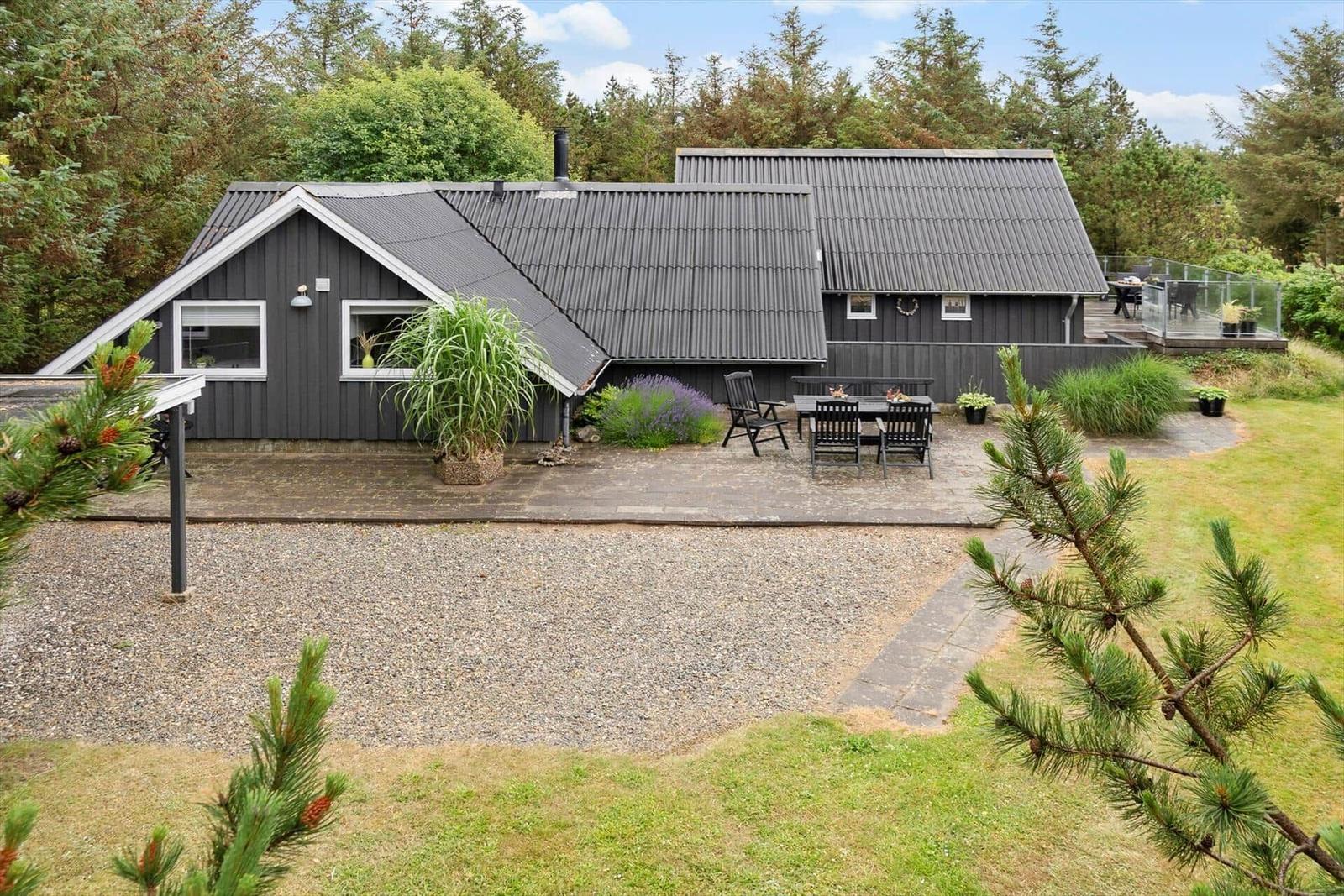Ein dunkelgraues Haus mit Terrasse und Garten inmitten von Bäumen.