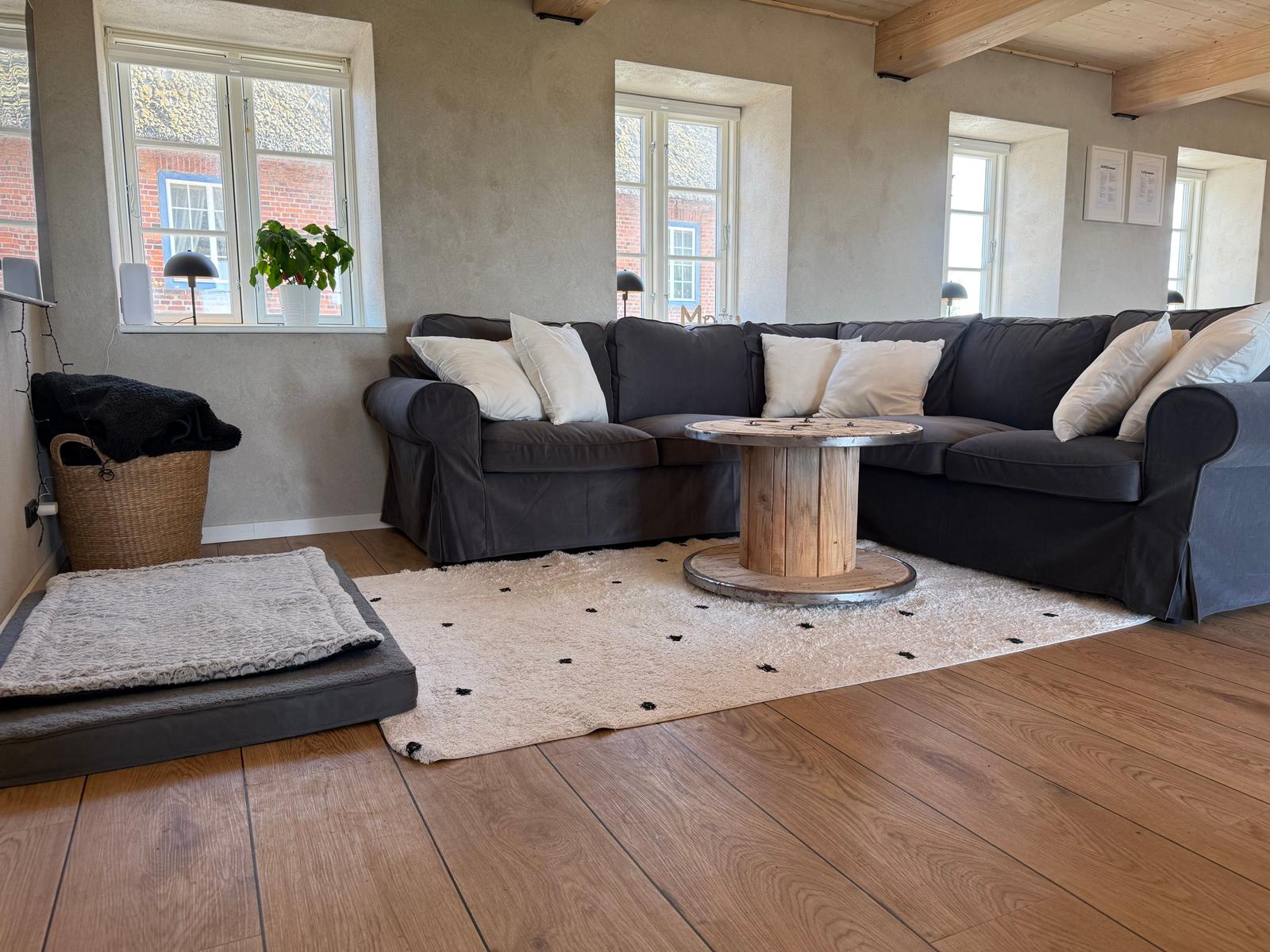 Großer Wohnbereich mit dunklem Sofa, Holzboden und runden Tisch.