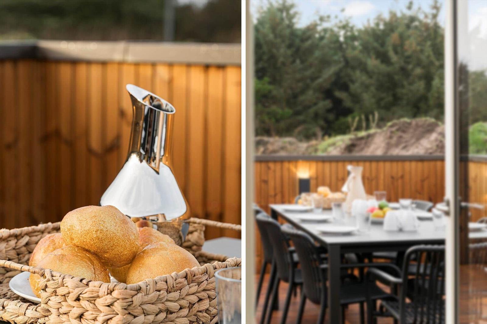 Außenbereich mit Tisch, Stühlen und Brotkorb. Hintergrund: Holzgeländer und Bäume.