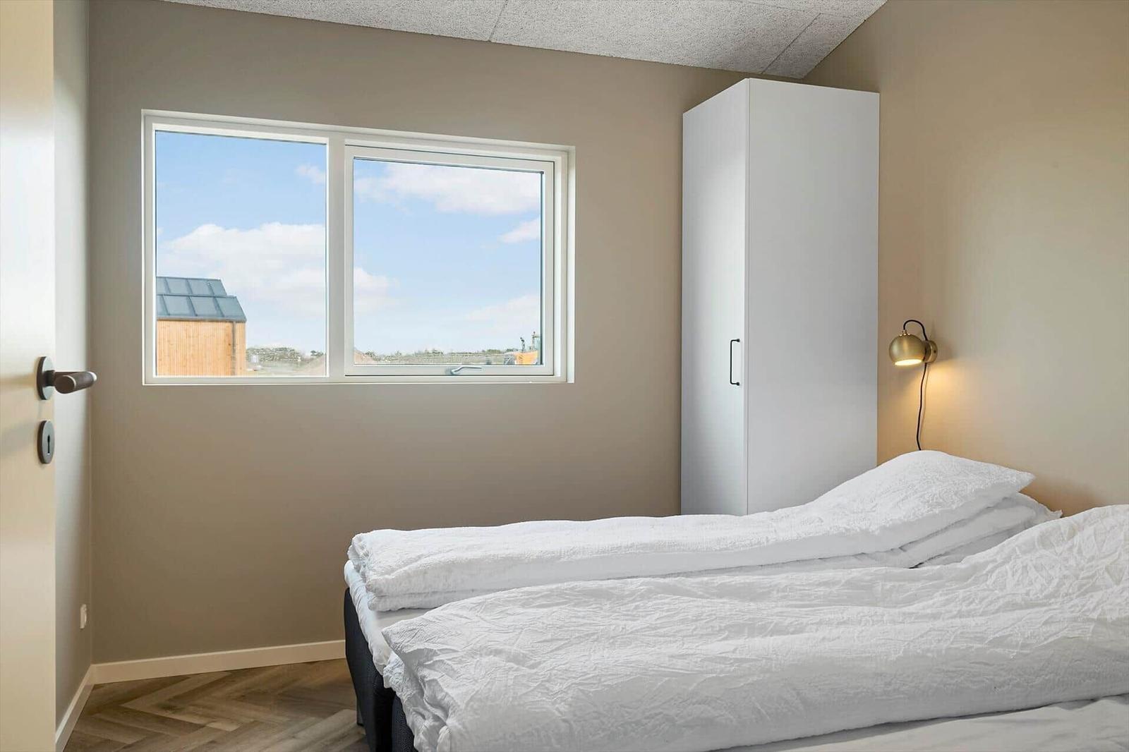 Schlafzimmer mit Bett, Kleiderschrank und Fenster mit Blick nach draußen.