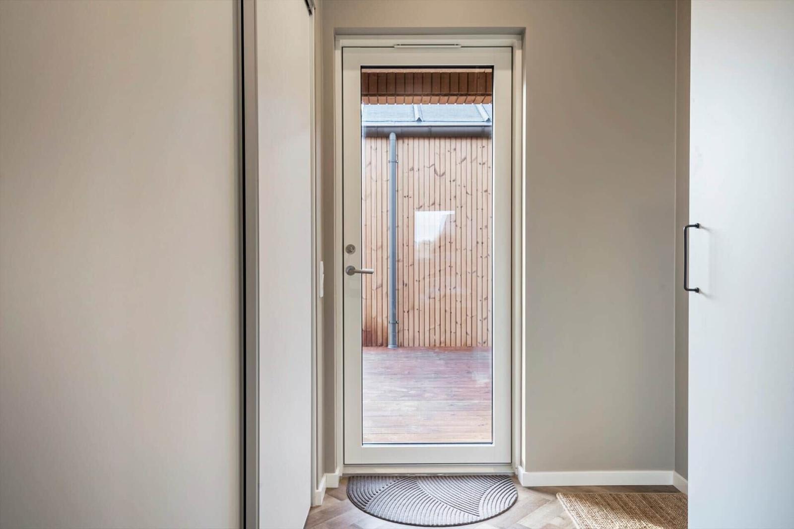 Eingangstür mit Glasfront führt auf eine Holzterrasse mit Holzwand.