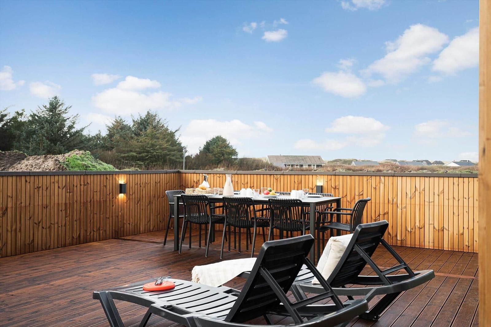 Terrasse mit Tisch, Stühlen und Liegen. Holzgeländer und Blick auf Grünland.