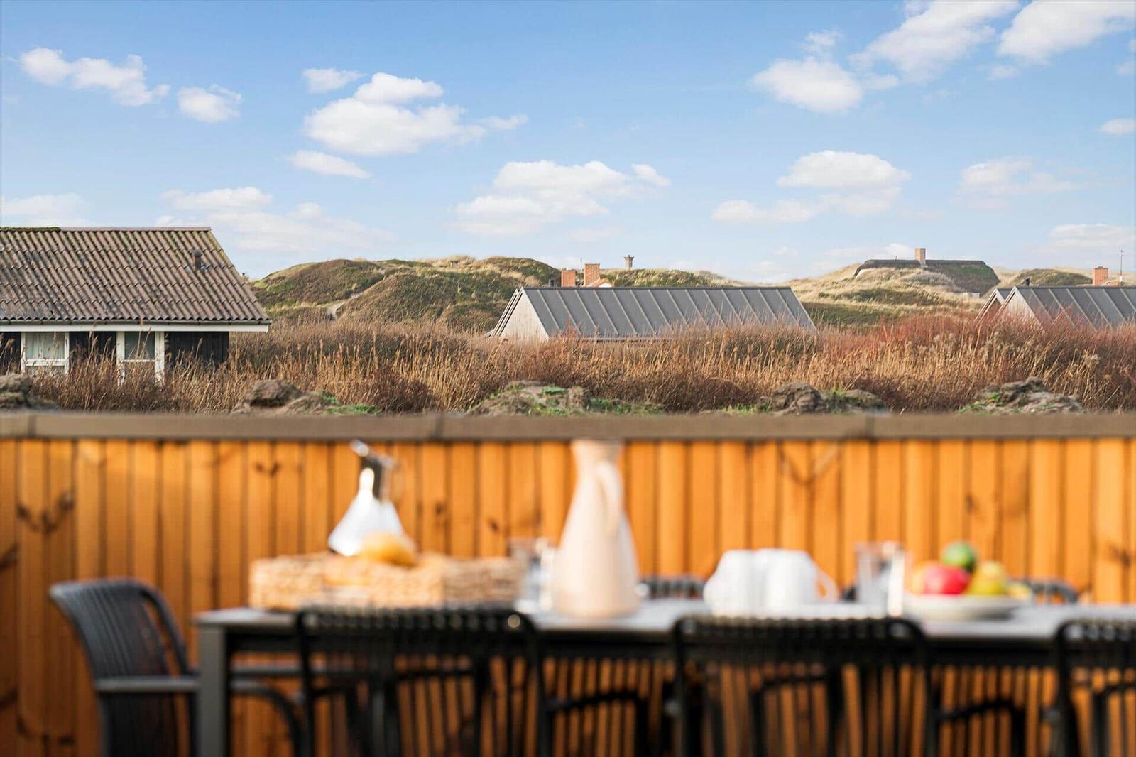 Terrasse mit Tisch und Stühlen, Blick auf Dünenschutz und Häuser im Hintergrund.