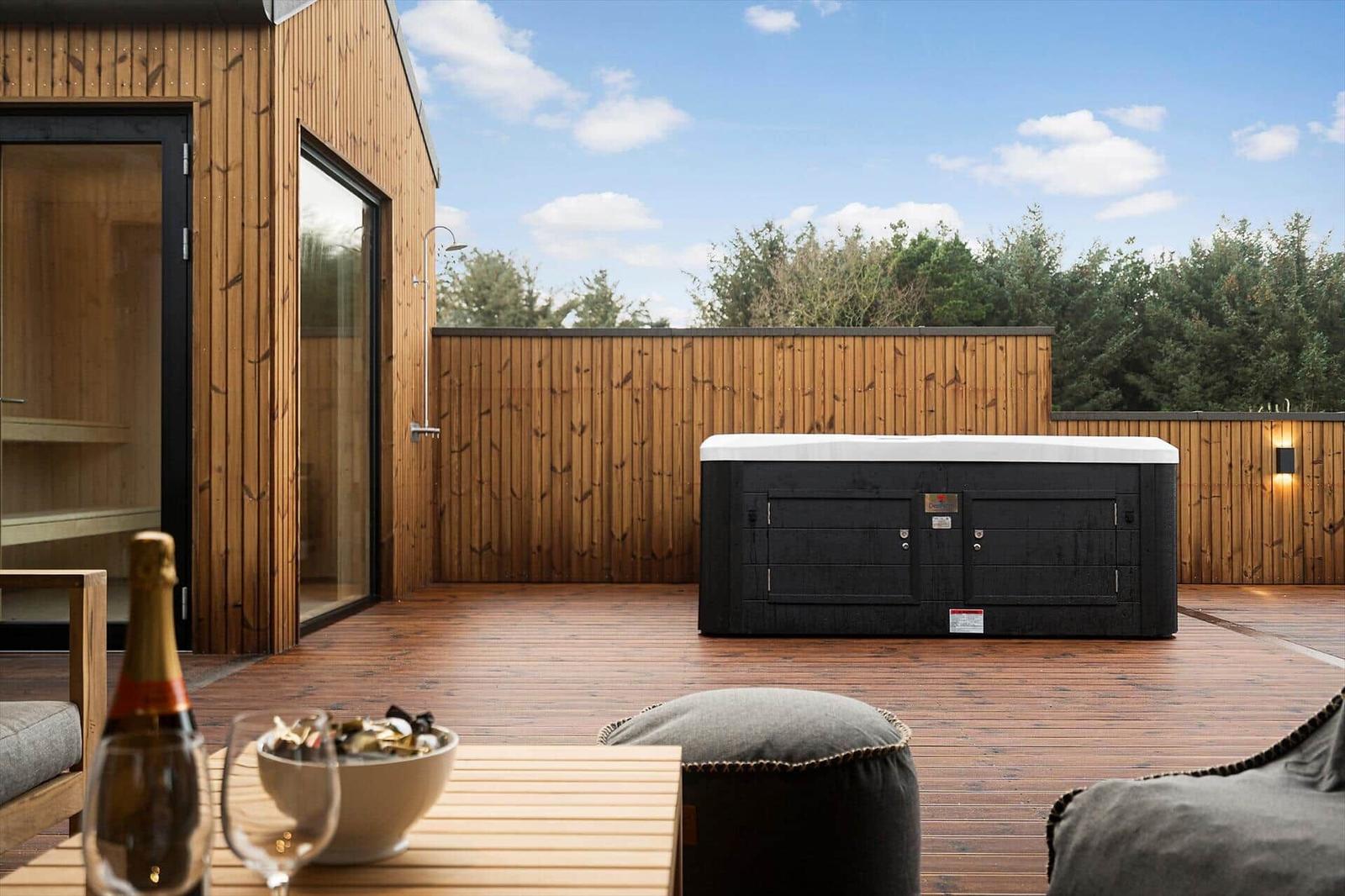 Terrasse mit Whirlpool, Holzwand und Sitzgelegenheiten. Flasche Champagner und Gläser auf Tisch.