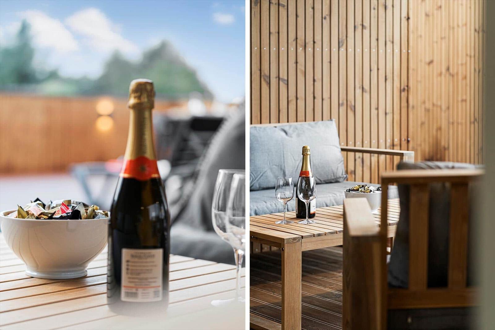 Terrasse mit Holztisch, Flasche Sekt und Gläsern vor Holzwand