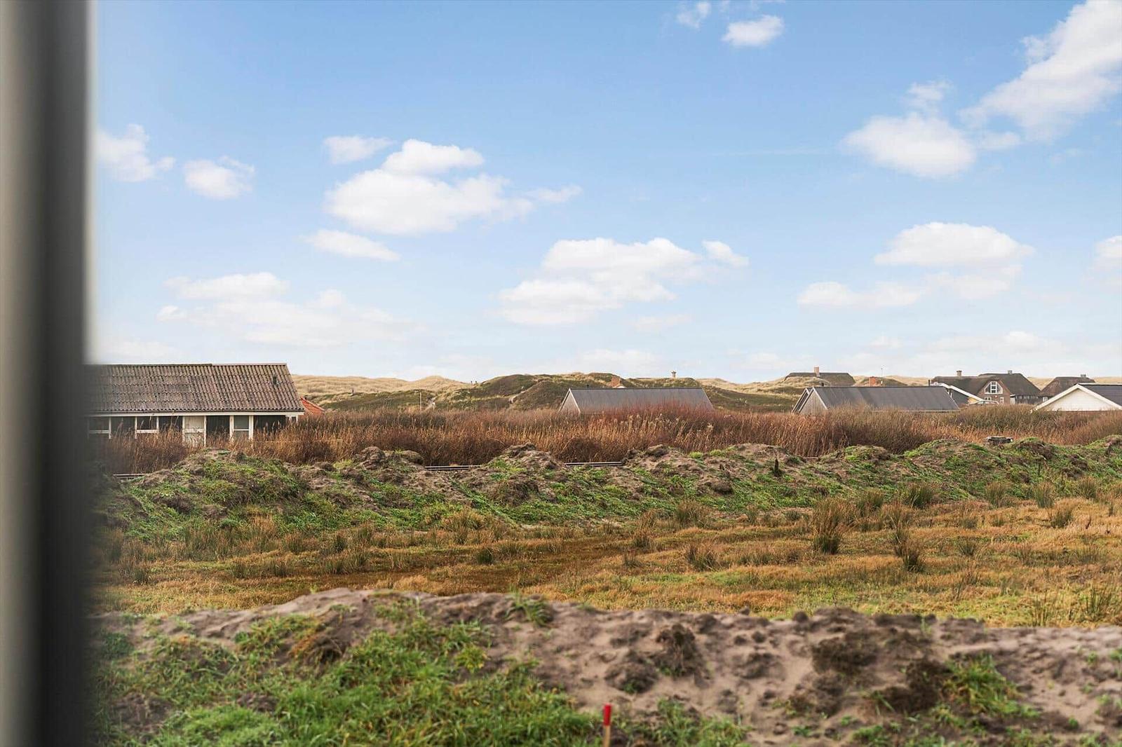 Aus dem Fenster blickt man auf eine Wiese mit Häusern und Dünen im Hintergrund.
