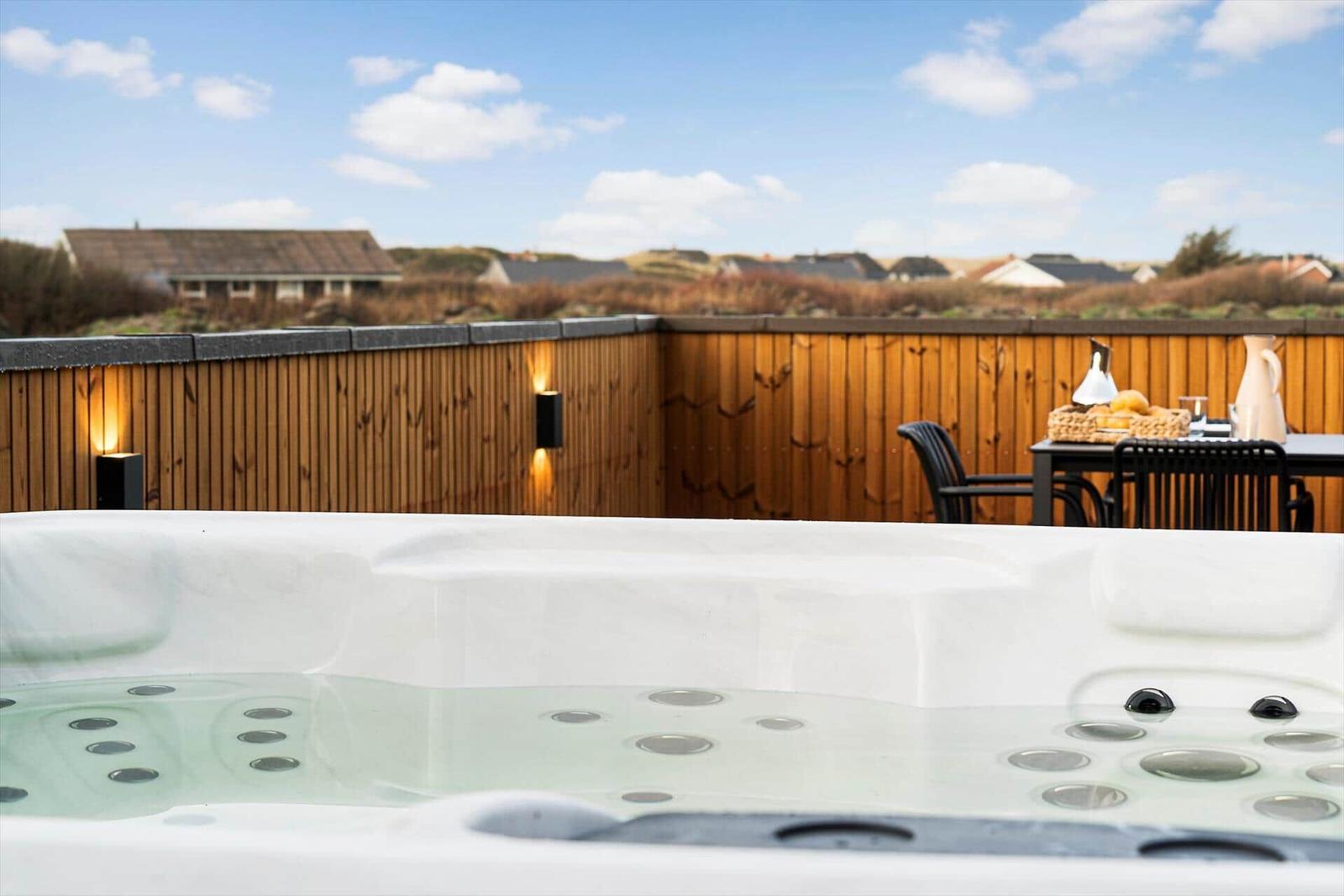 Eine Außenterrasse mit Whirlpool, Holzgeländer und Tisch mit Stühlen.