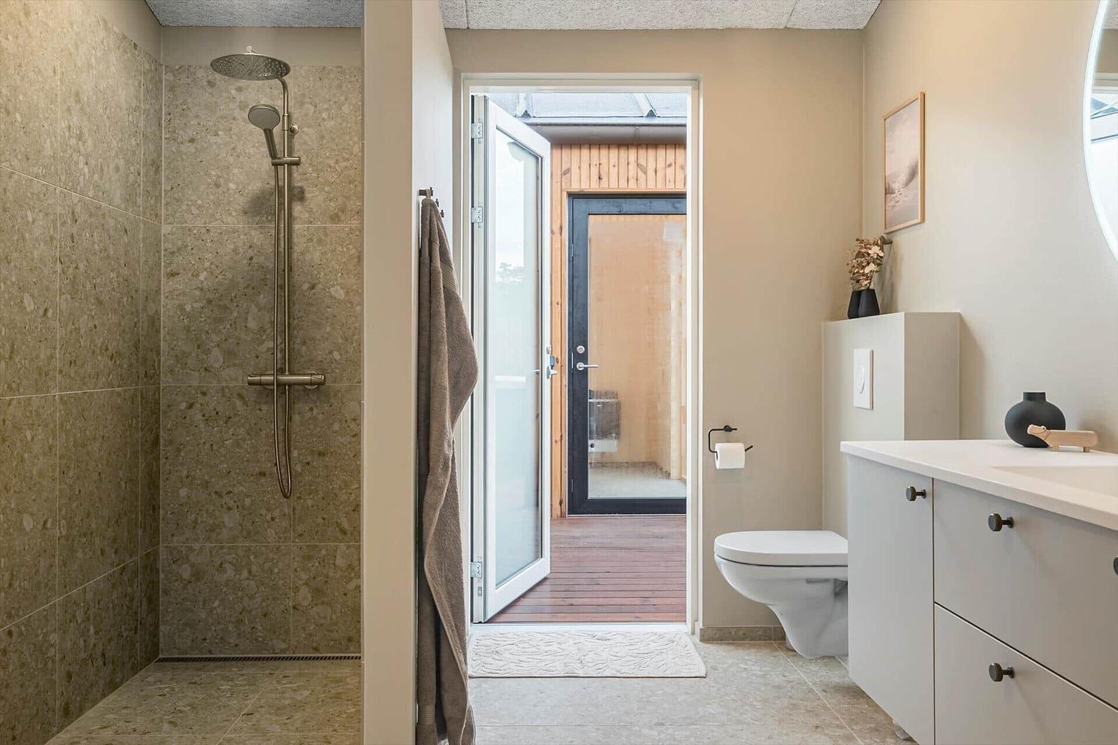 Bad mit Dusche, Toilette und Waschbecken. Durchgang zur Terrasse mit Holzdecke.