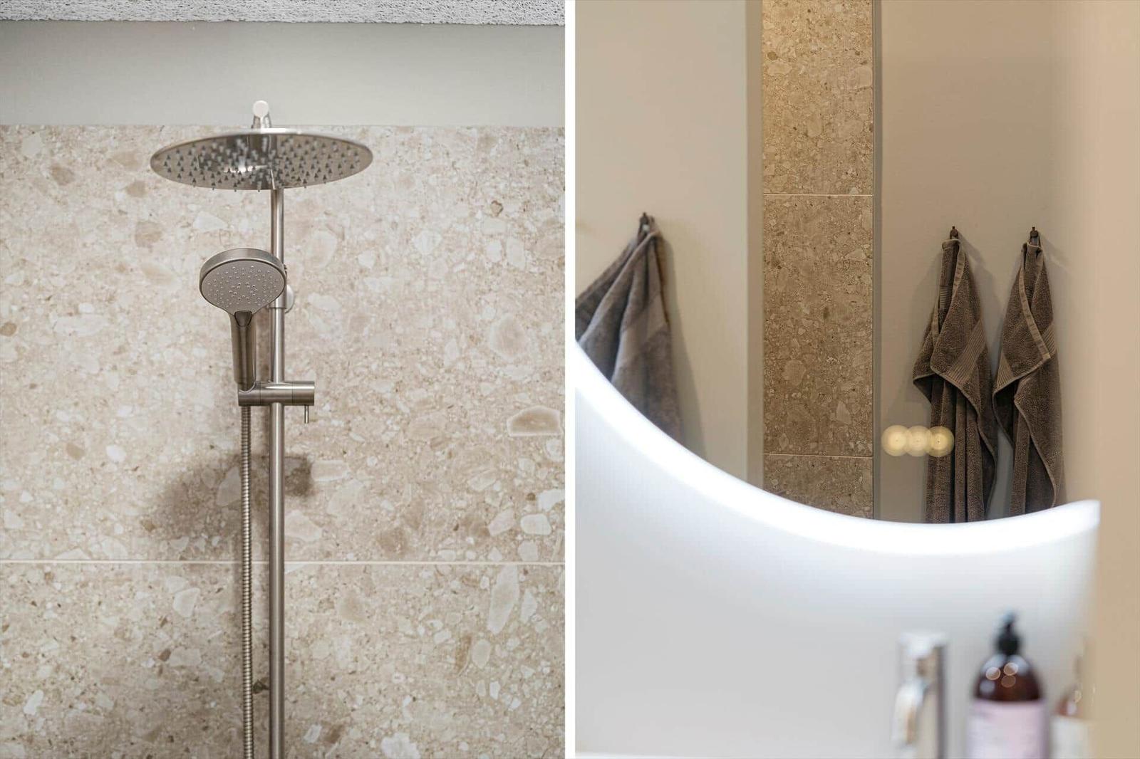 Duschkopf und Handbrause an Terrazzowand. Spiegel mit Handtüchern und Waschbecken.
