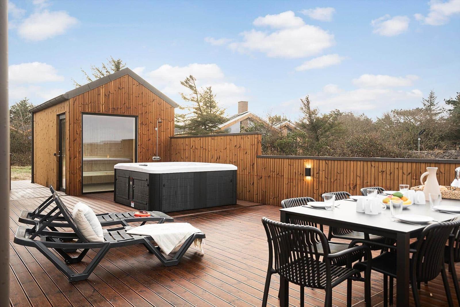 Terrasse mit Sauna, Whirlpool, Liegestühlen und Esstisch.