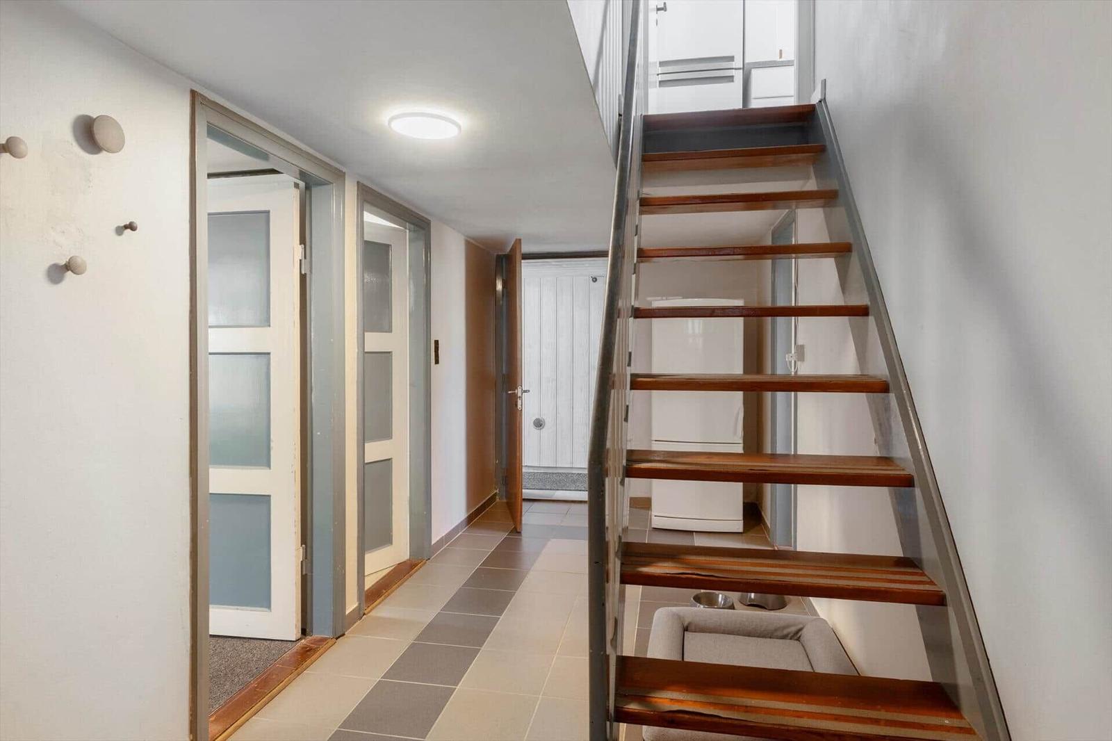 Hallway with wooden staircase, door, and refrigerator visible