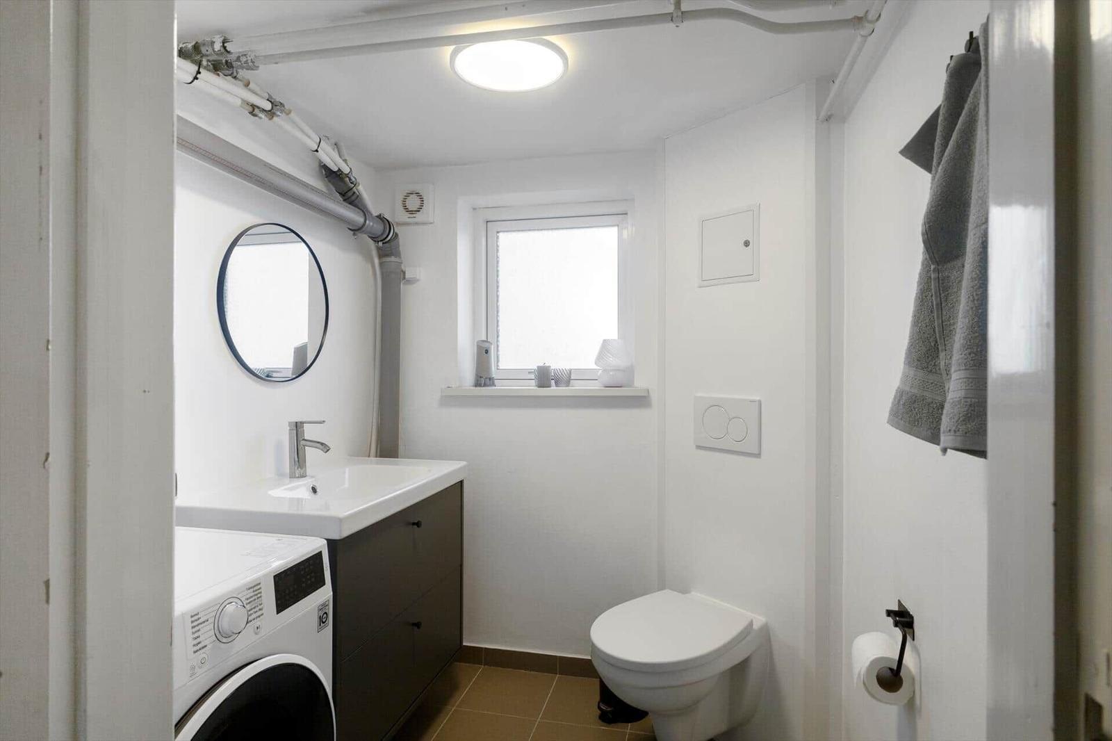 Bathroom with washing machine, toilet, and round mirror