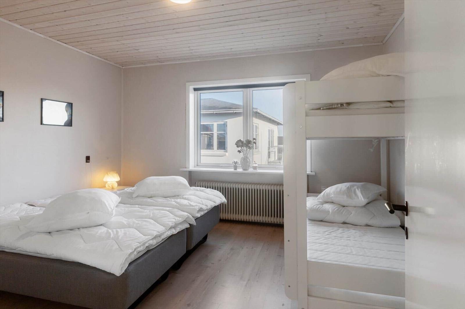 Room with double bed and bunk bed, window, wooden floor, and white walls.