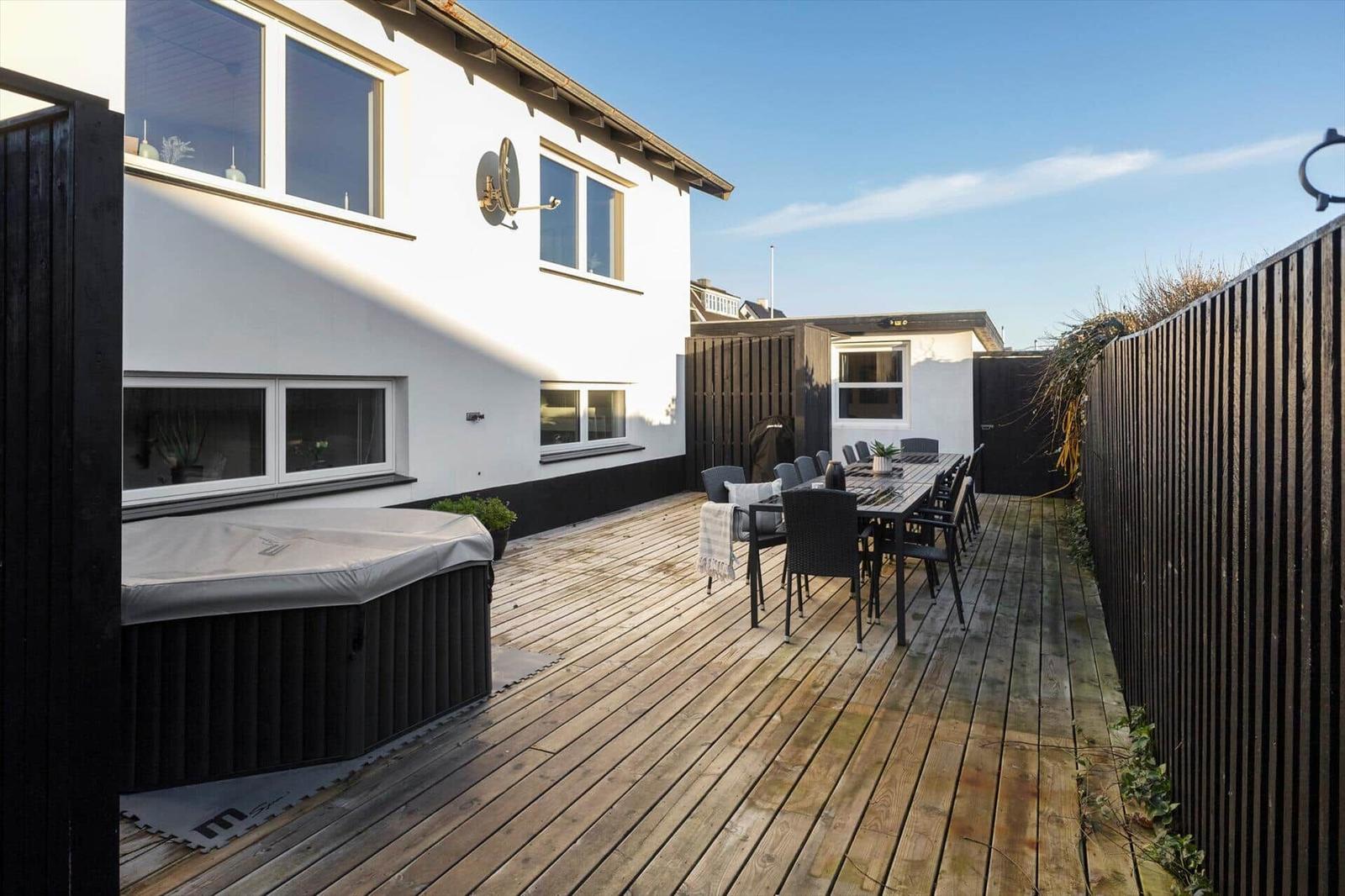 Deck with wood, seating group, and hot tub. Backyard with fence and house.