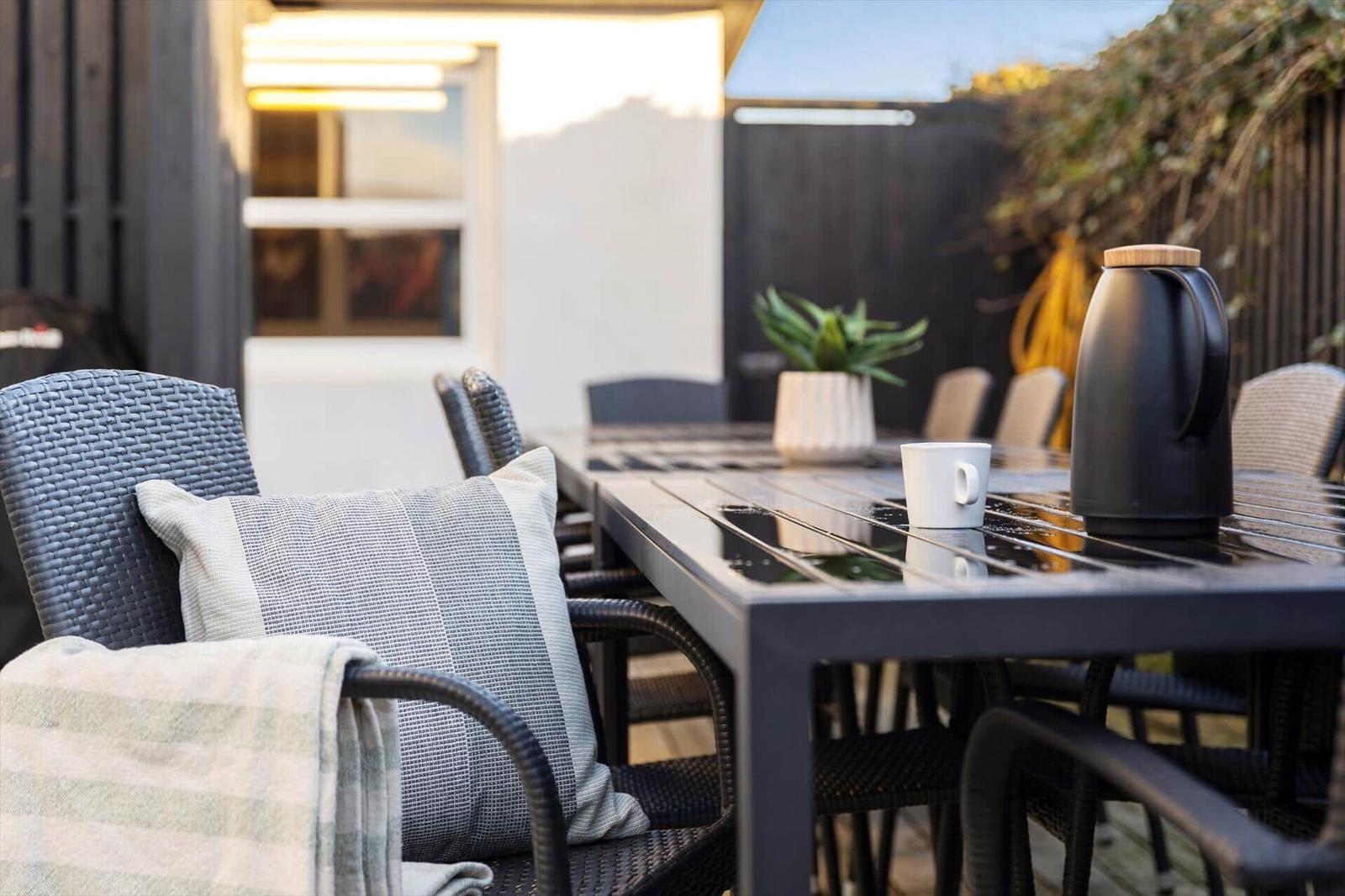 Outdoor area with table, chairs, cushions, and thermos.