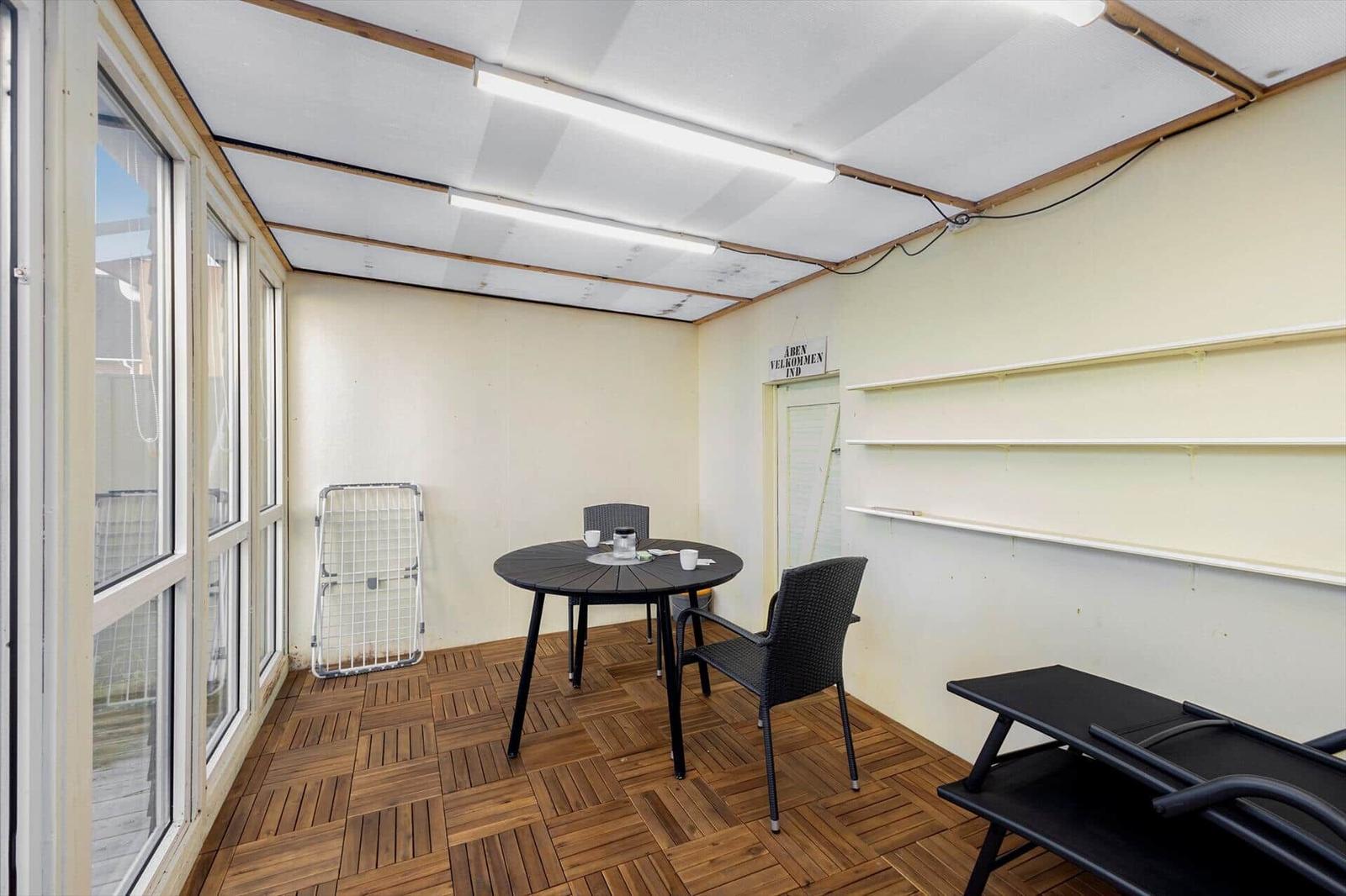 Terrace with table, chairs, and lounge chair. Wooden floor and window front.