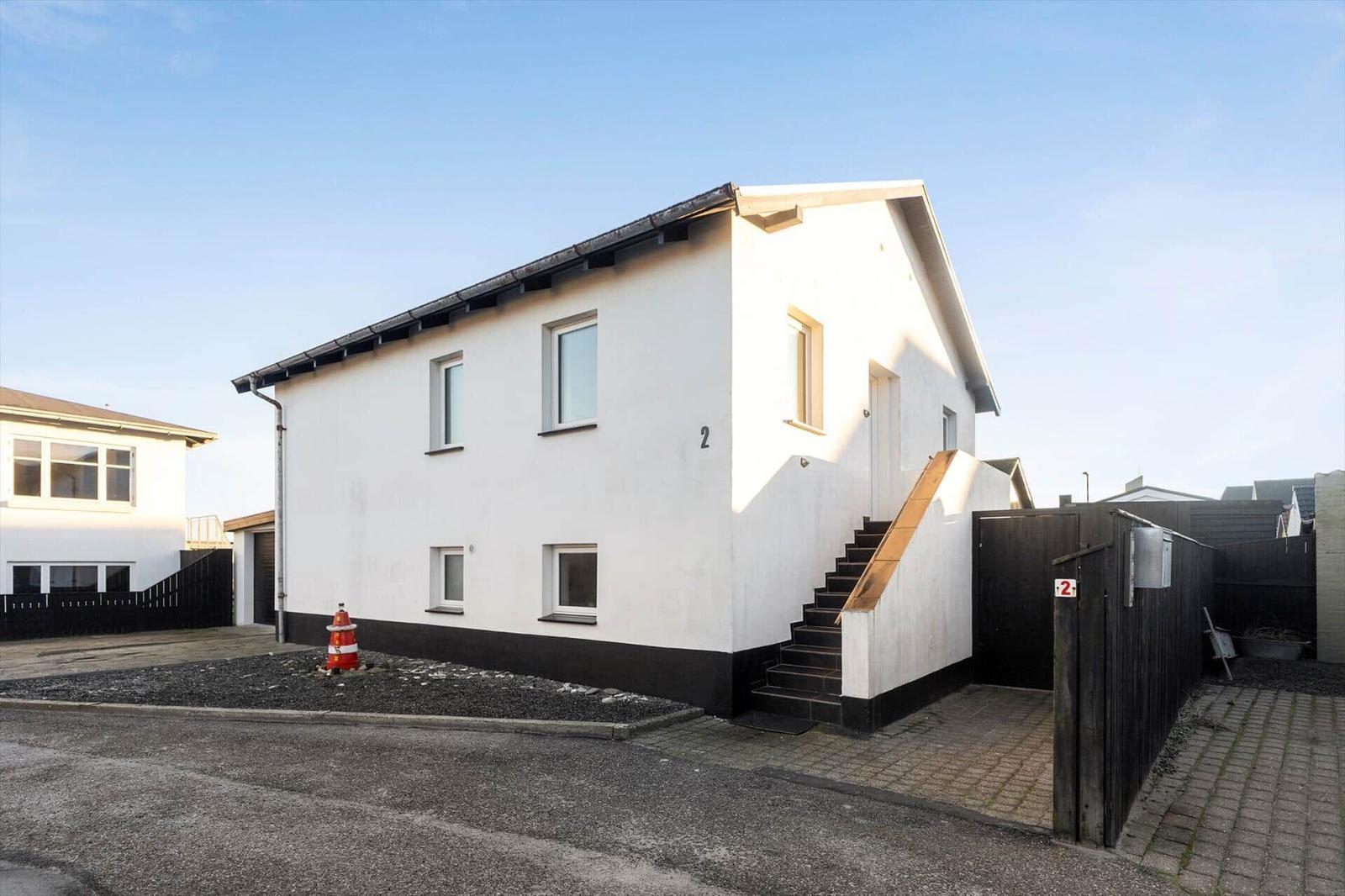 Modern house with white walls and black base, entrance stairs and garden fence.