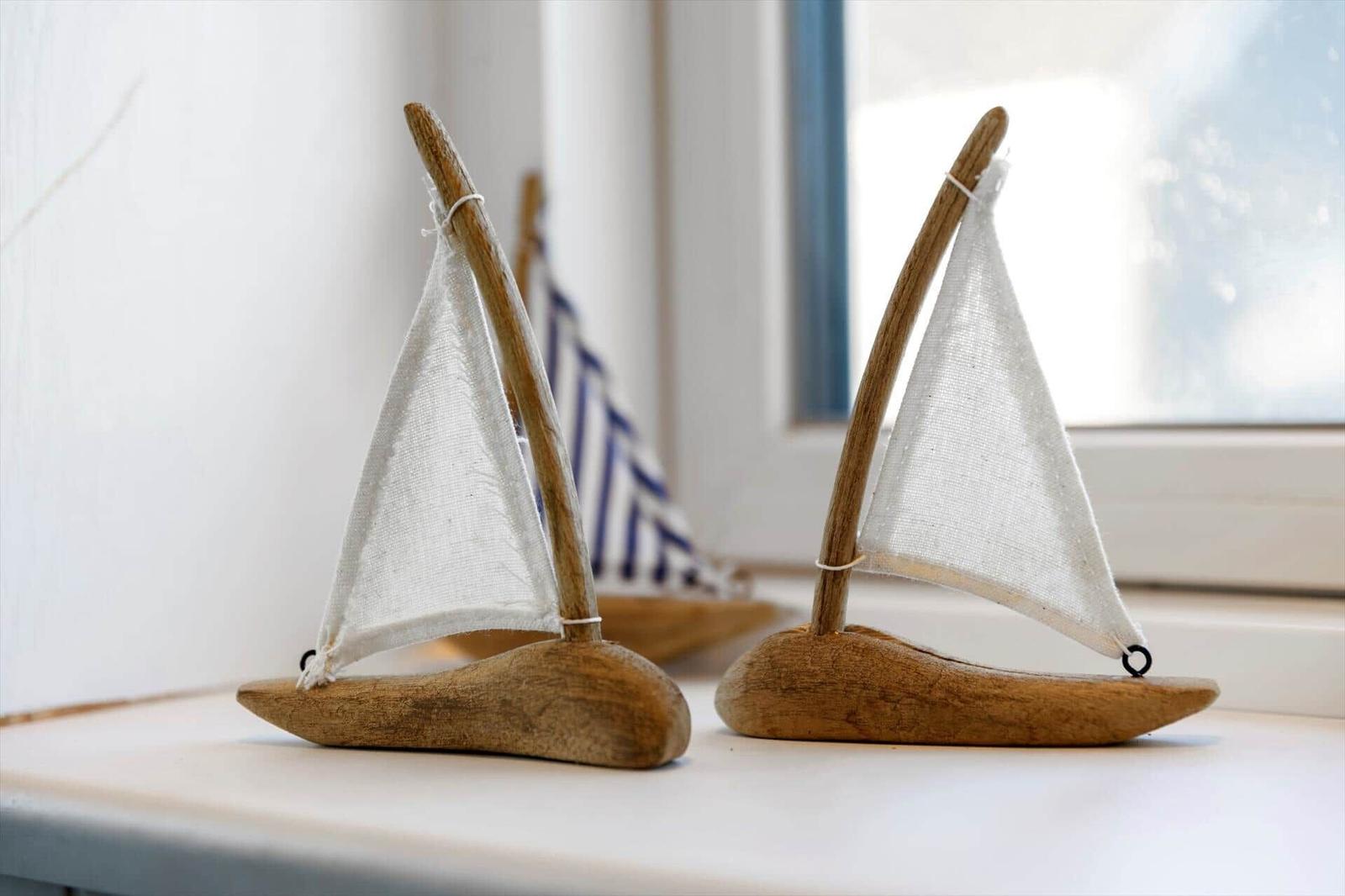 Two wooden sailboats with white sails are on a windowsill.