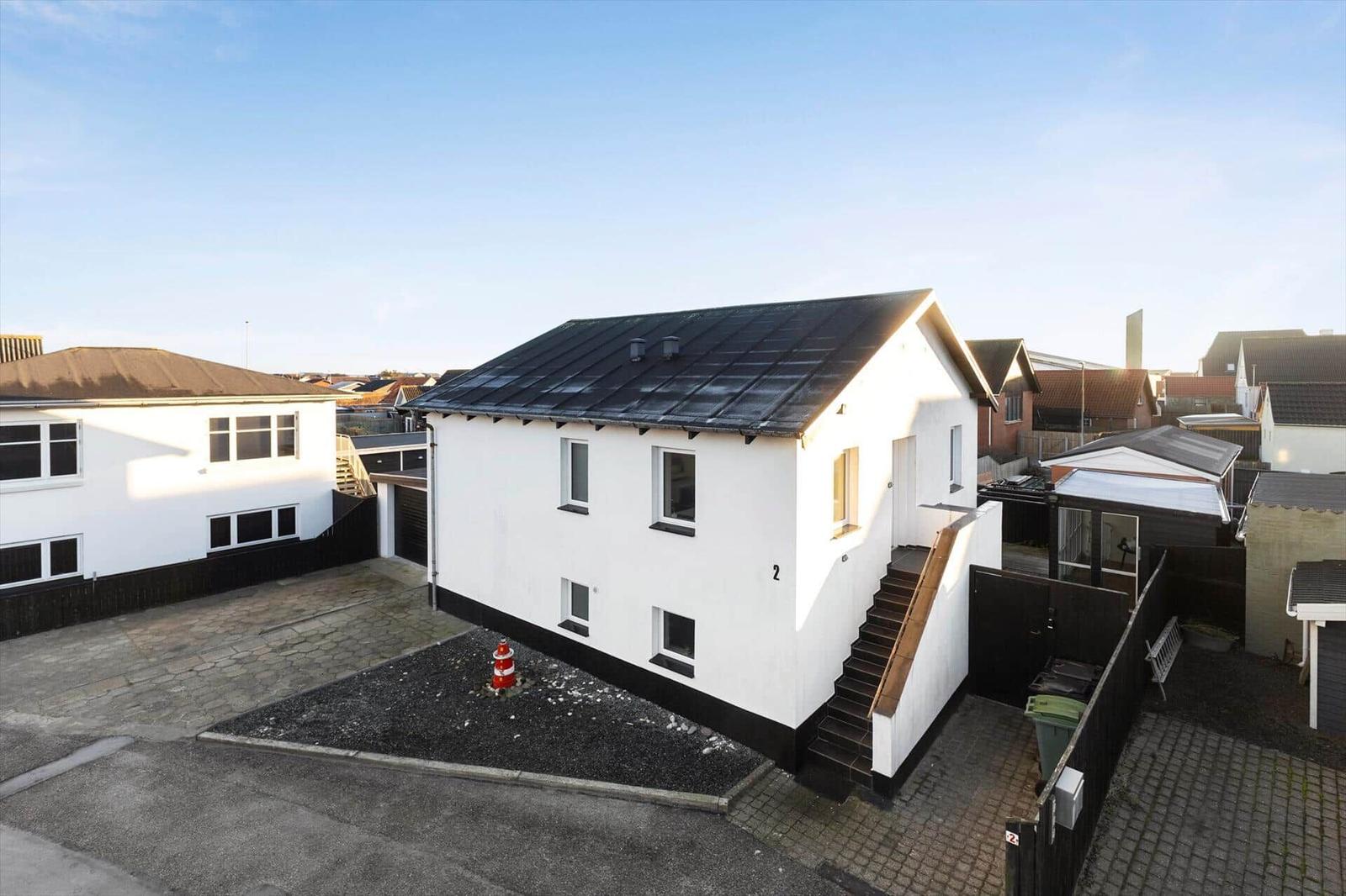 A white house with a black roof and outdoor stairs.