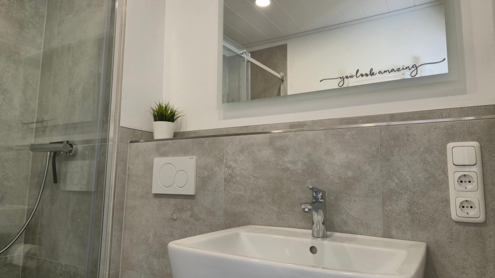 Bad mit Dusche, Waschbecken und Spiegel mit Aufschrift.