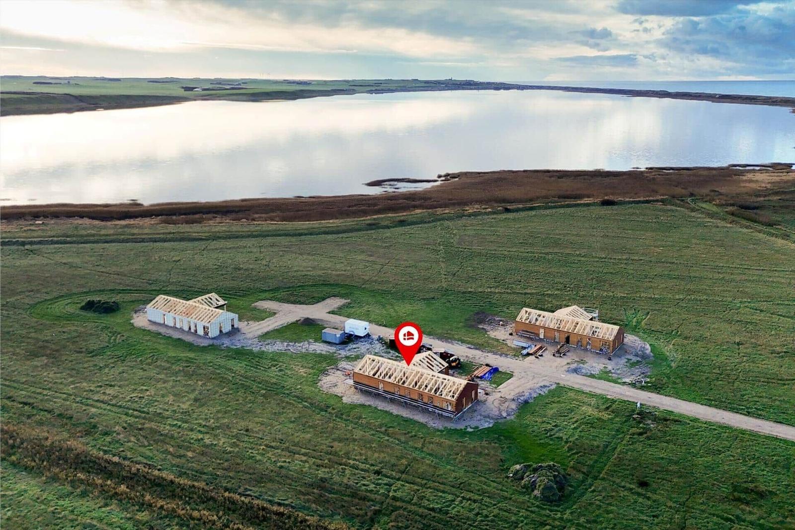 Drei Häuser in Bau auf einer grünen Wiese neben einem See.