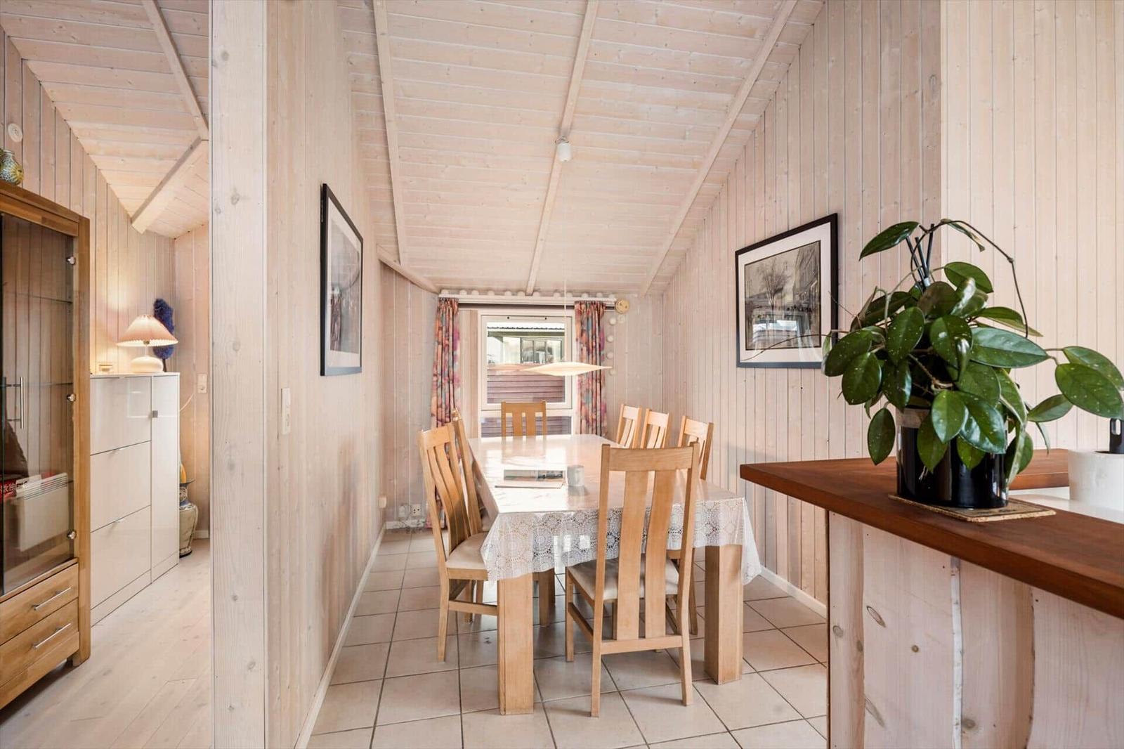 Dining room with wooden walls and table with chairs. Plant on kitchen island.