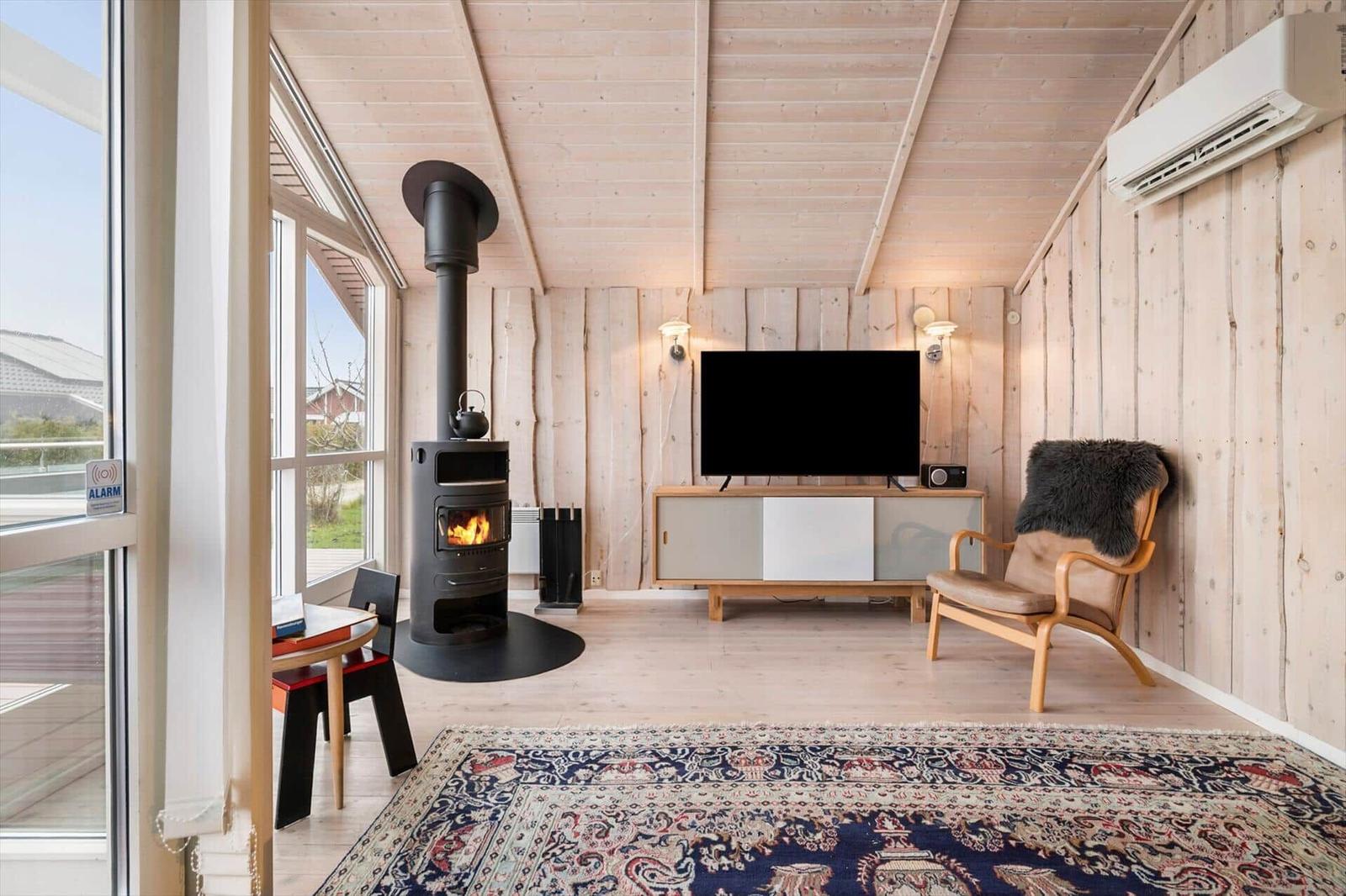 Living room with fireplace, TV, and armchair. Wooden walls and large windows.