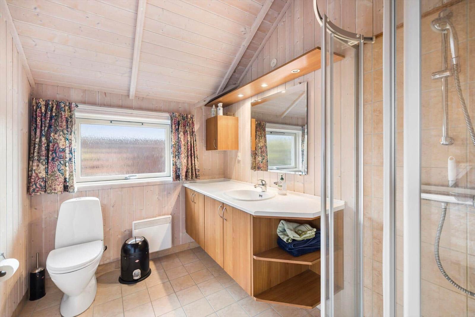 Bathroom with shower, sink and toilet. Wooden walls and window with curtains.