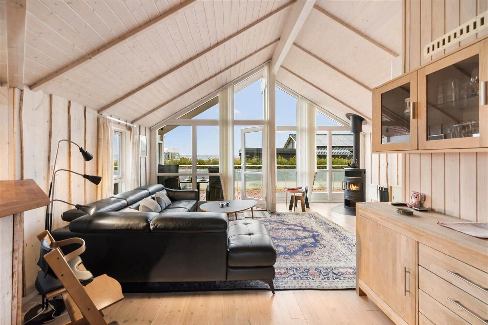 Living room with wooden walls, sofa, stove, and large window view.