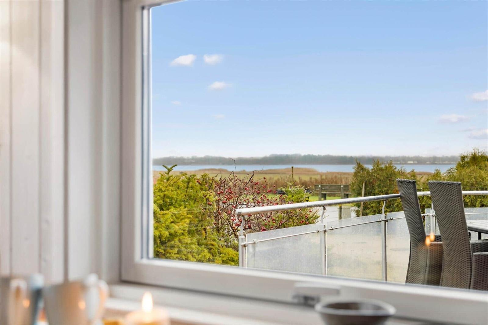 From the window, you can see a terrace with garden furniture and a lake.